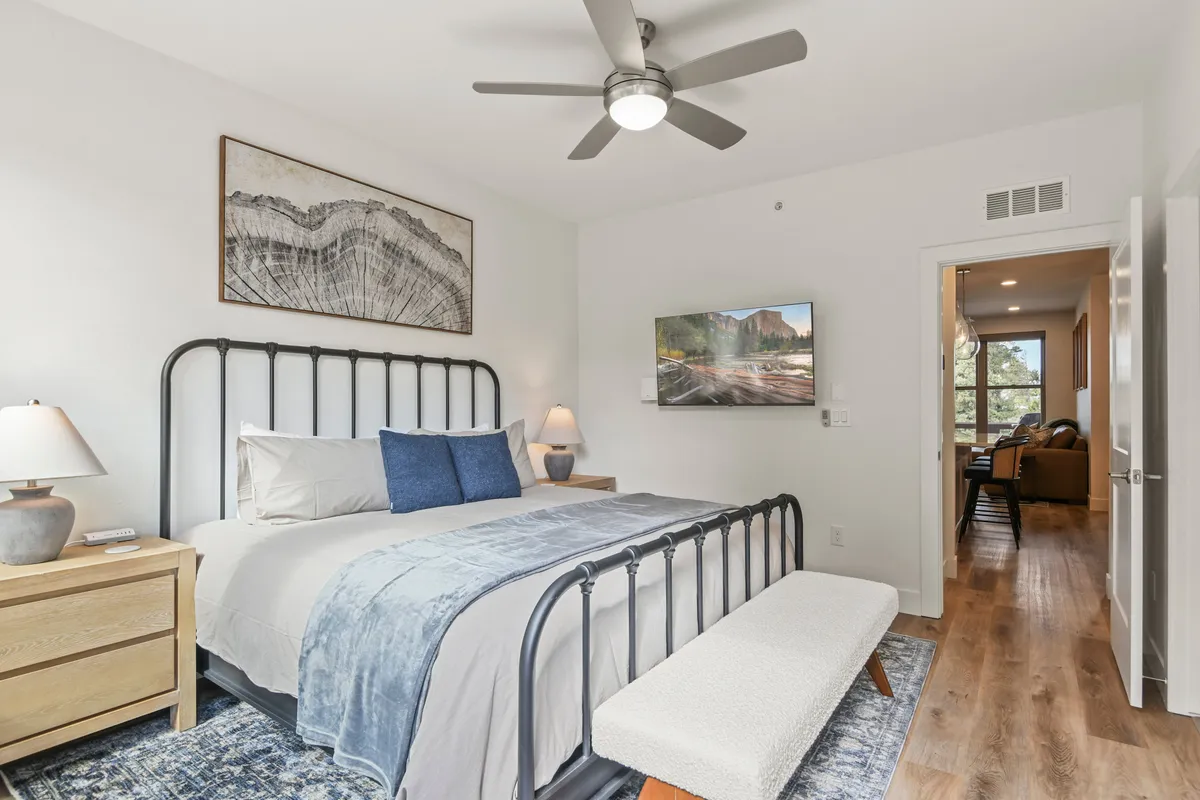 A beautifully styled king suite bedroom featuring a plush bed with decorative pillows, a bench at the foot, soothing artwork on the wall, and a nightstand with a lamp. The TV displays a serene landscape, contributing to a tranquil environment for rest and relaxation.