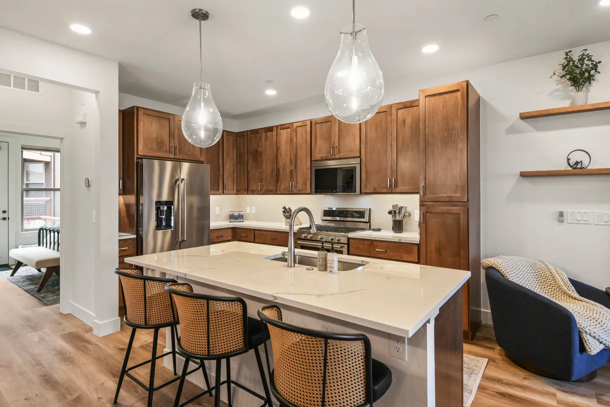 A contemporary kitchen featuring a spacious island with hanging pendant lights above, sleek stainless steel appliances, and ample counter space. The area is styled for both cooking and entertaining, evoking a sense of culinary inspiration and community gathering.