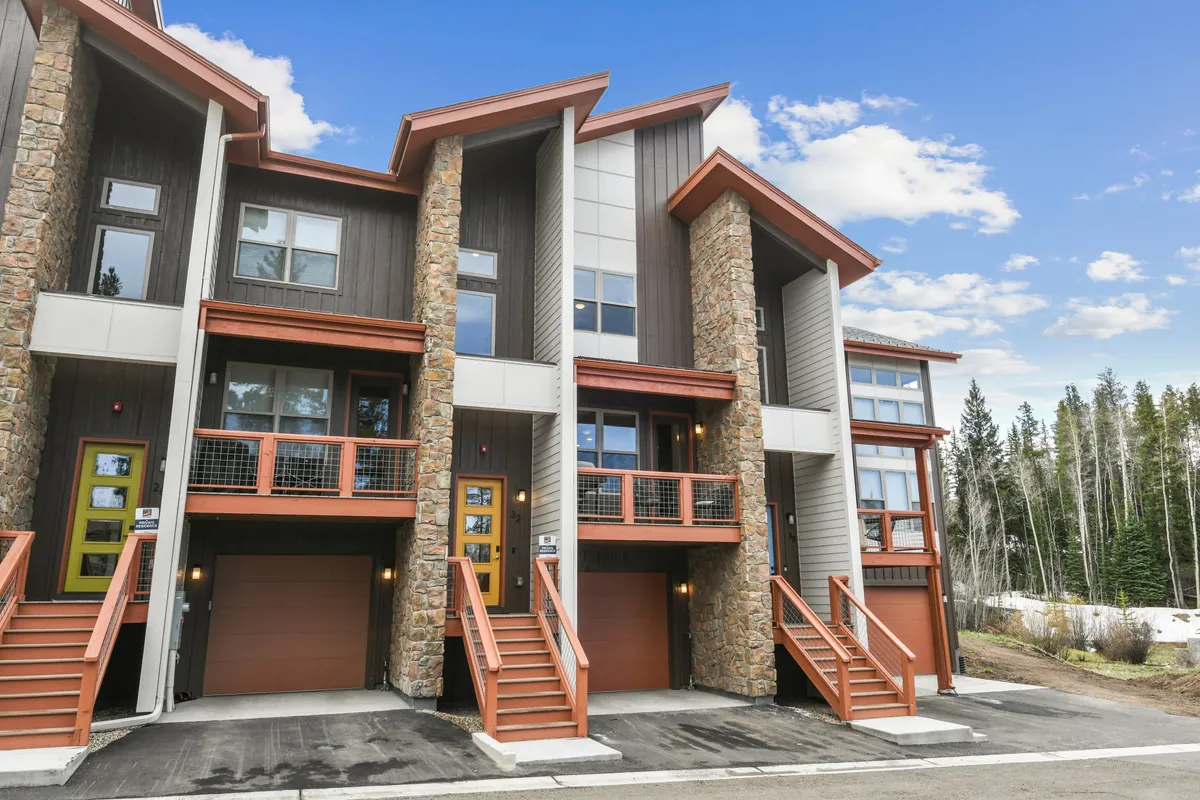 A welcoming exterior shot of the chalet featuring a stone façade, red-accented stairs and doors, and large windows. The porch invites relaxation and social gatherings, set against a backdrop of natural beauty.