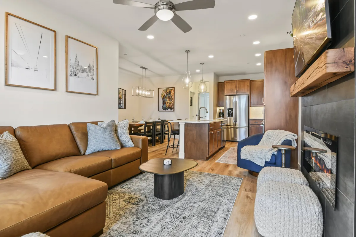 A warm, open interior with a stylish leather sofa facing a fireplace, a dining area visible in the background, and modern decor that blends comfort and elegance. There’s ample space for entertaining, sharing meals, and gathering as a group, with ambient lighting creating a welcoming mood.