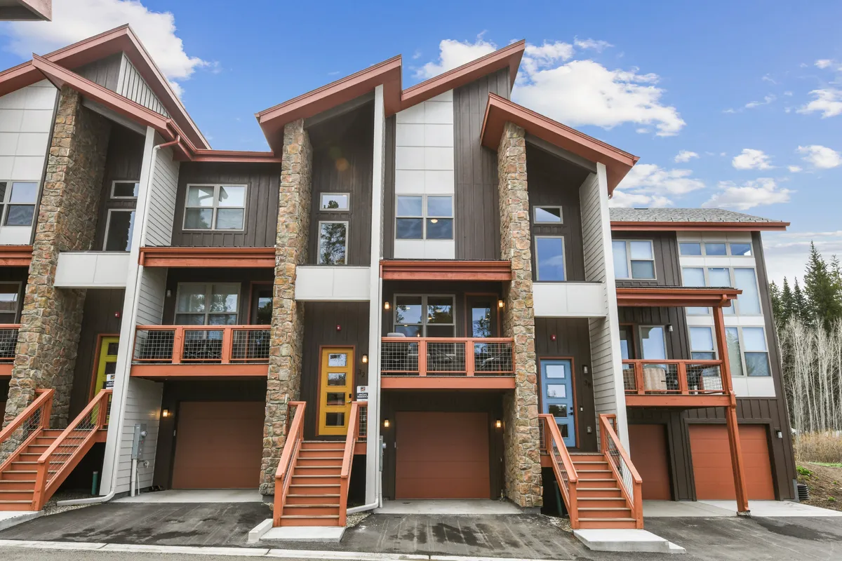 A welcoming exterior view of the vacation home, featuring a stone facade, angled roofs, colorful doors, and balconies. The image is bathed in soft sunset light, creating a warm and inviting atmosphere. The balconies hint at spaces for morning coffee or evening relaxation, while the communal layout suggests a vibrant community.