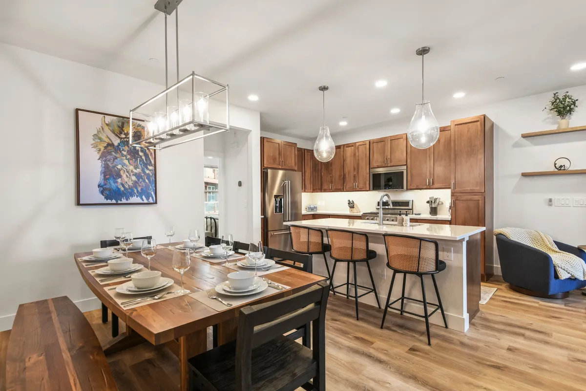 A warm dining area that seamlessly connects to the kitchen, showcasing a large, inviting table perfect for group meals. Artwork on the wall and natural lighting contribute to an ambiance ideal for both formal celebrations and casual breakfasts.